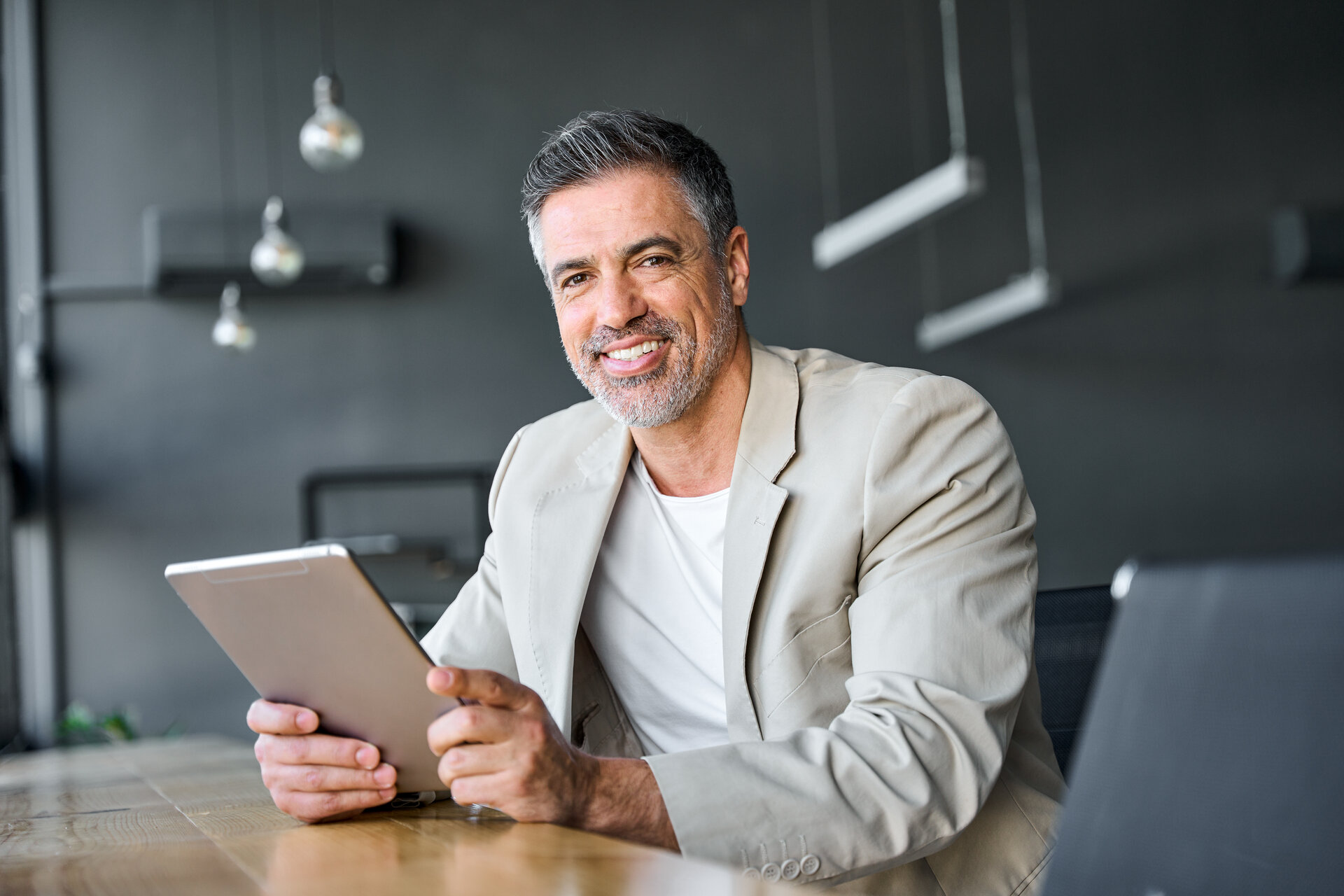 Geschäftsmann mittleren Alters mit digitalem Tablet in einem modernen Büro sitzend. Porträt