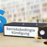 Ein Aktenordner mit der Aufschrift „Betriebsbedingte Kündigung“, daneben eine goldene Waage und ein Paragrafensymbol – Symbolbild für Abfindungen und Kündigungsrecht.