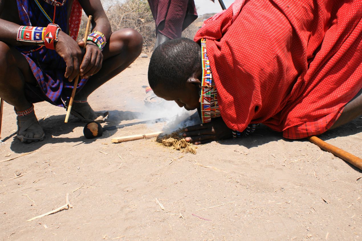 Massai-Krieger beim Entzünden eines Feuers in der Savanne, traditionelles Erlebnis während einer Tansania Safari