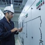 Techniker mit Helm und Tablet kontrolliert Schaltschrank in technischer Umgebung – Einsatz von Glasfaser Adapter in mittelstaendischer Infrastruktur