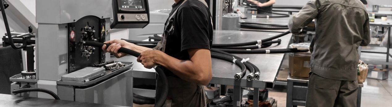 Mitarbeiter fertigt Chemieschläuche an einer Maschine, weitere Schlauchleitungen liegen auf Werkbänken bereit